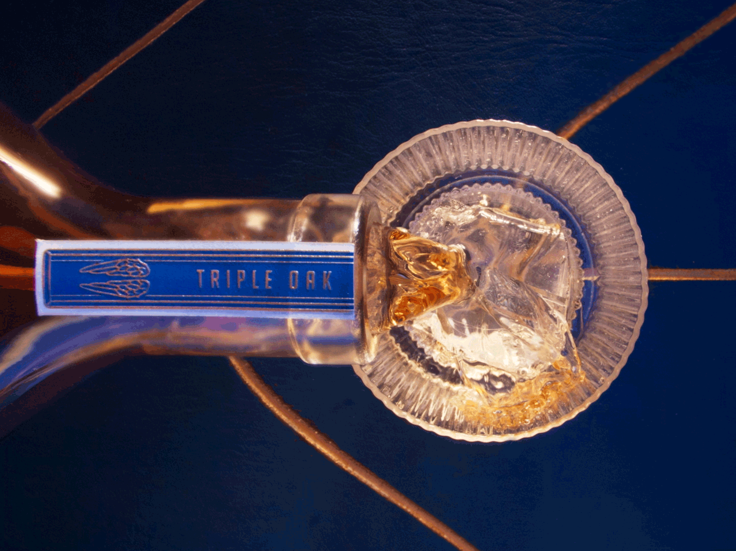 Angel's Envy Triple Oak bourbon bottle pouring over ice in a glass, showcasing its rich amber color.