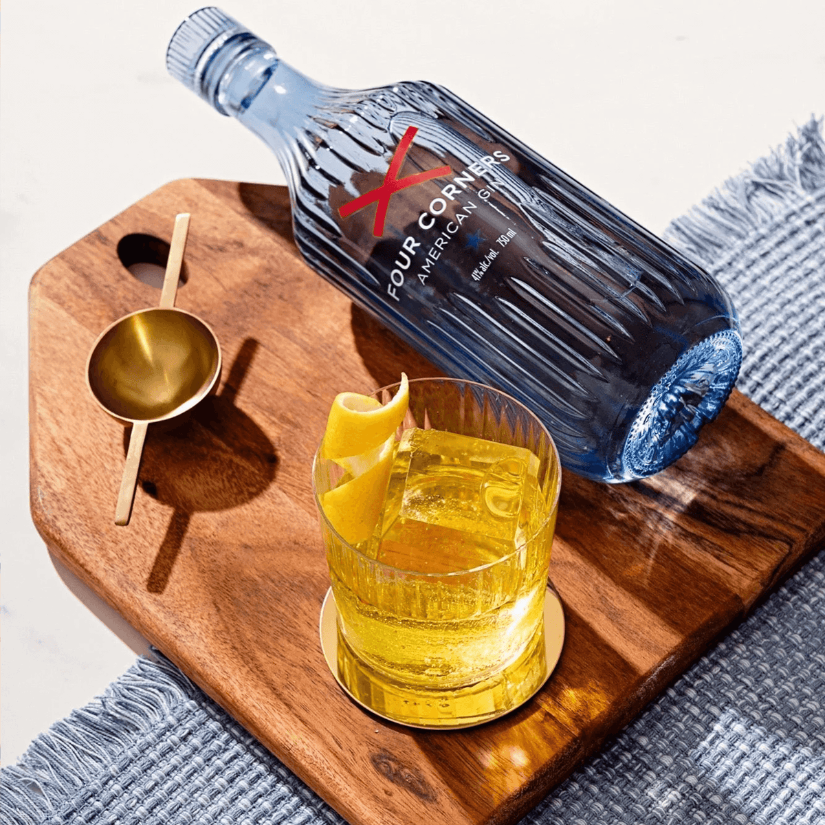 Four Corners American Gin bottle next to a glass of gin cocktail on a wooden serving board.