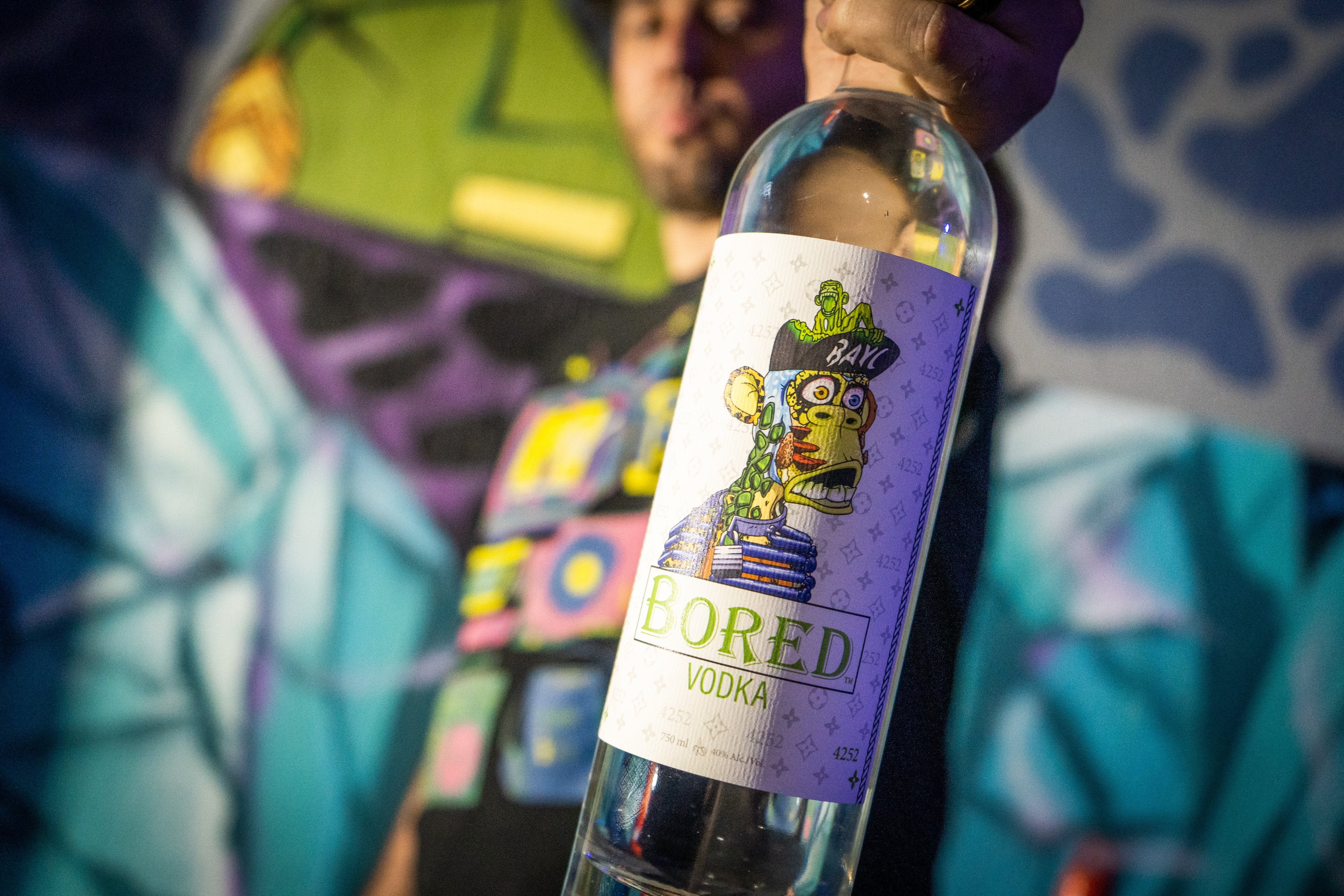 Bored Vodka bottle held up against a colorful mural background, showcasing modern art and craft distillation.