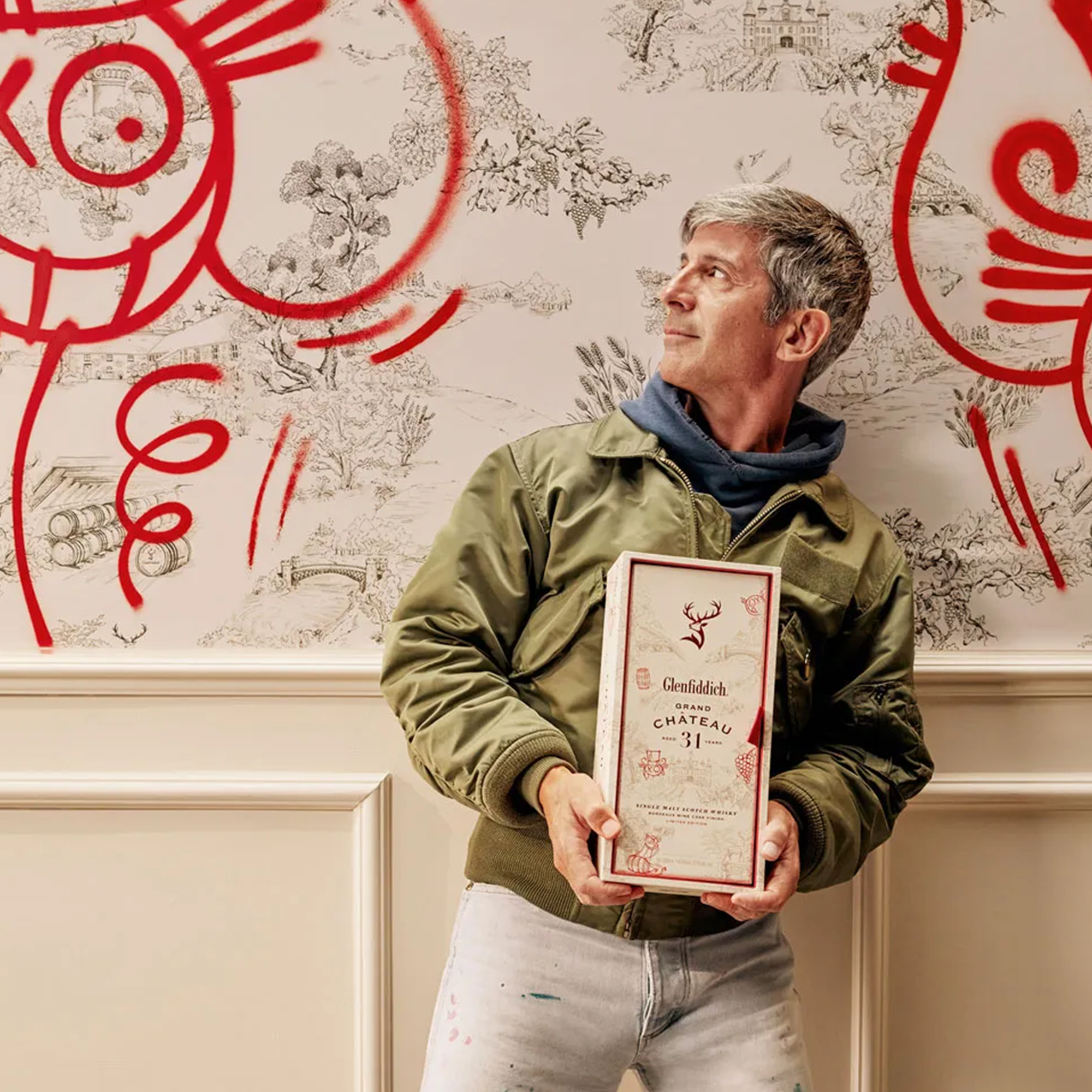 Man holding Glenfiddich Grand Château 31 Year Single Malt Scotch bottle against a decorative wall.