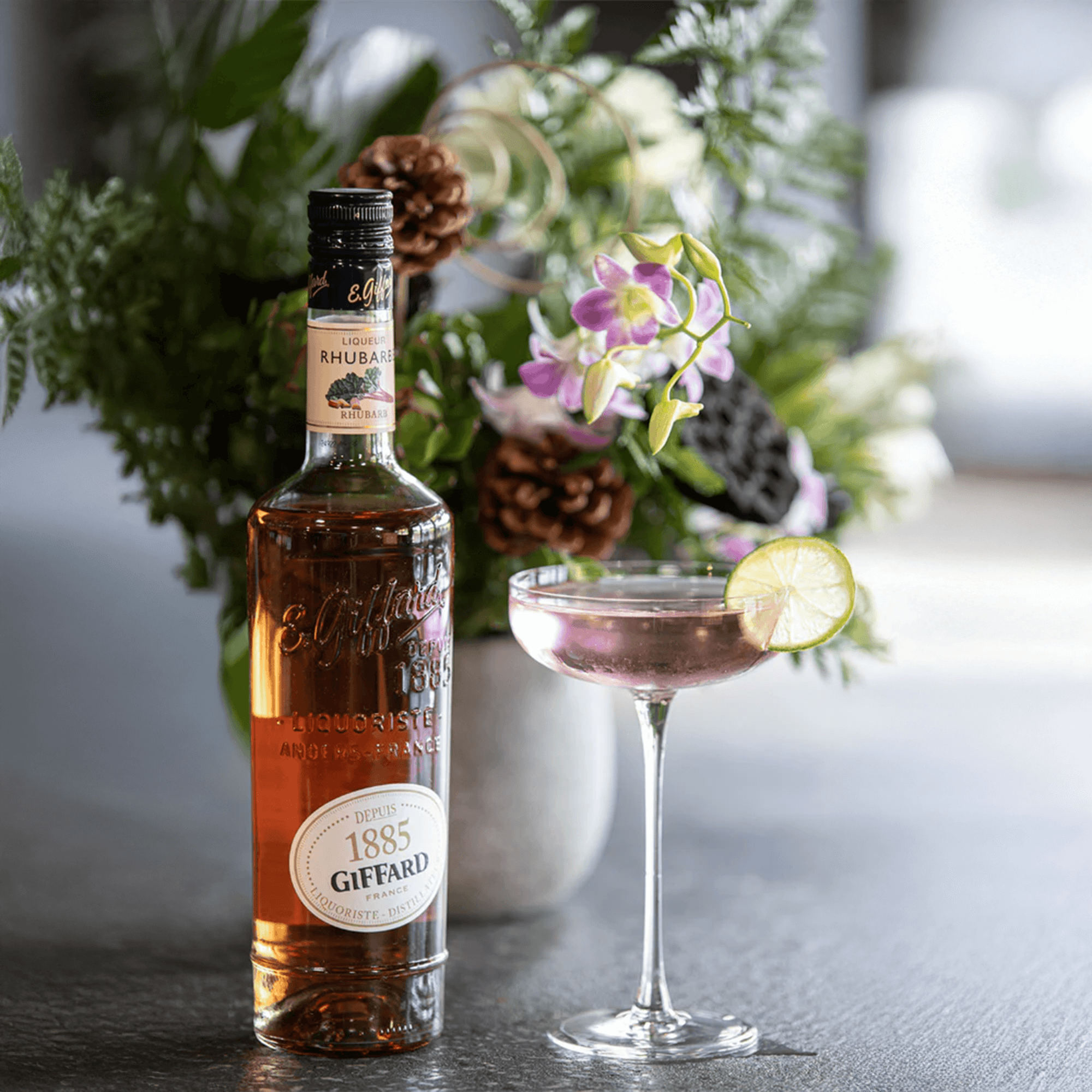 Giffard Rhubarb Liqueur bottle with a cocktail garnished with lime in a stylish setting.