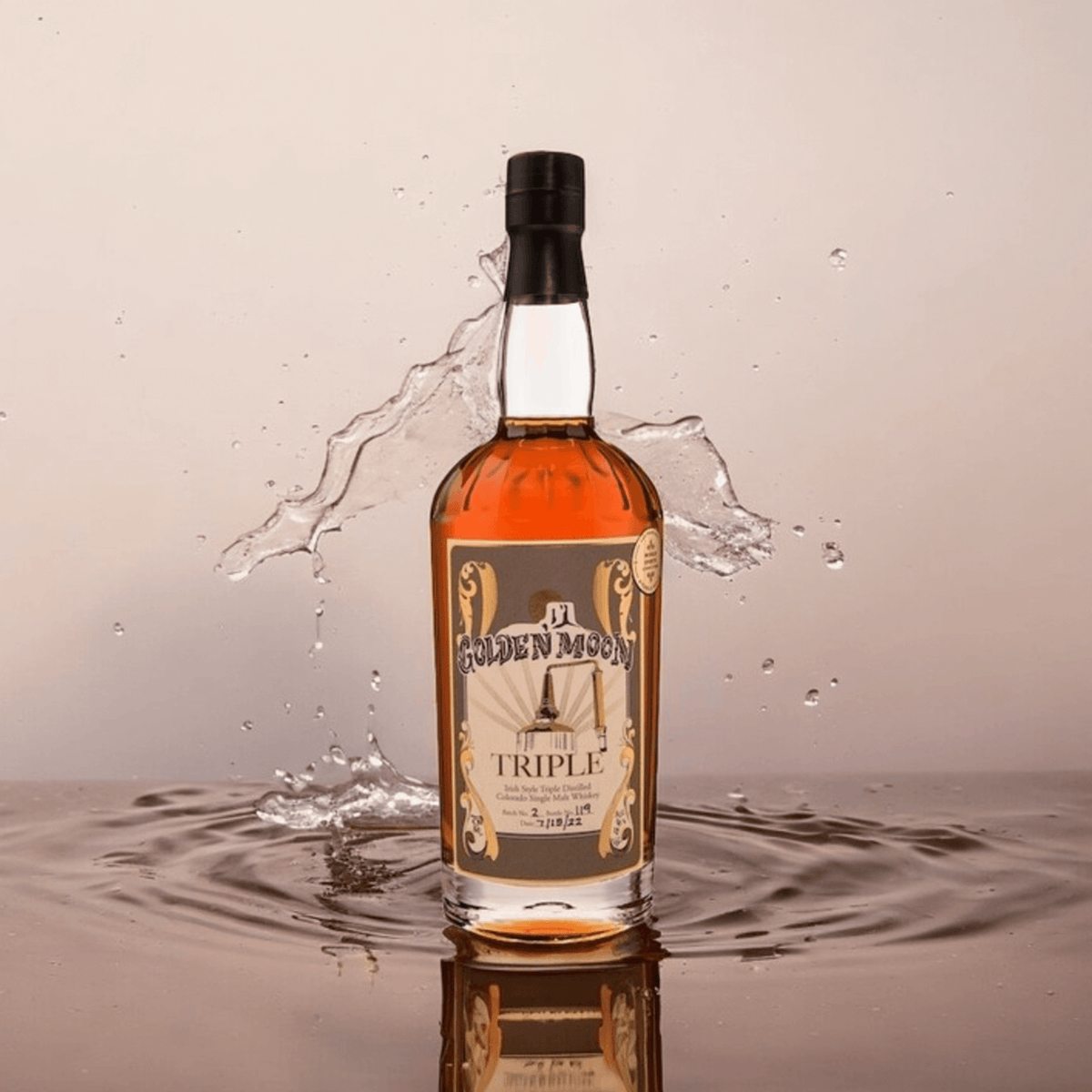 Golden Moon Triple Colorado Single Malt Whiskey bottle splashing in water, showcasing its rich amber color and unique design.
