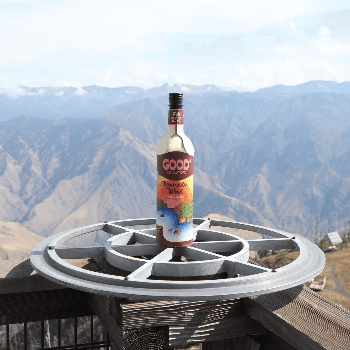 Good Distillations Weekender Wheat Whisky bottle on a scenic overlook with mountains in the background.