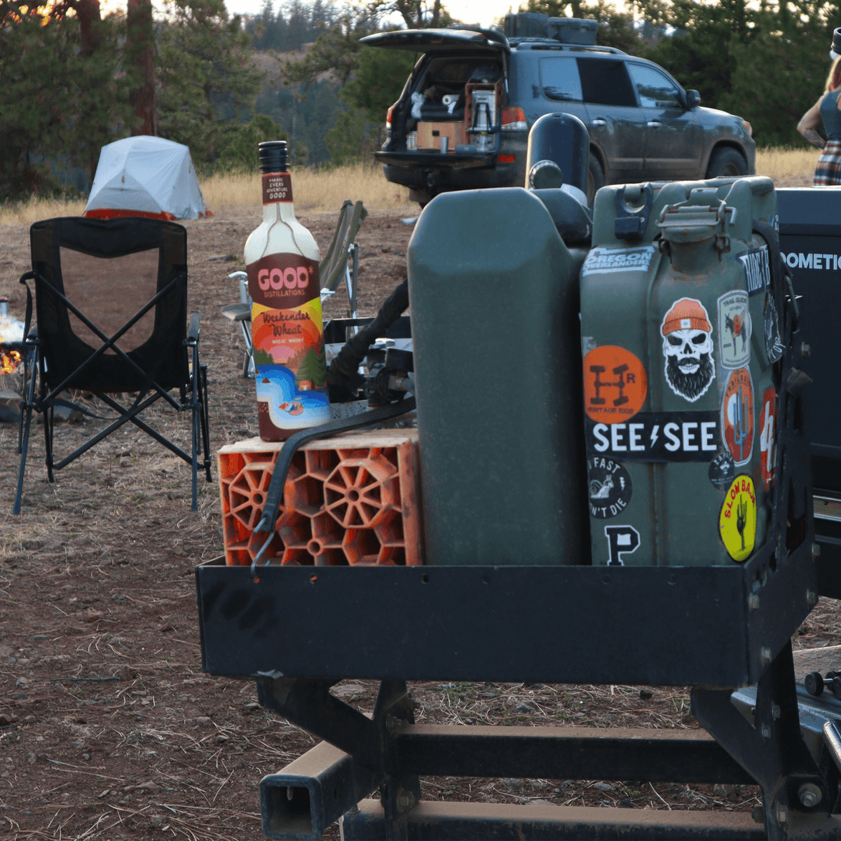 Good Distillations Weekender Wheat Whisky bottle on a camping table amid outdoor setting.