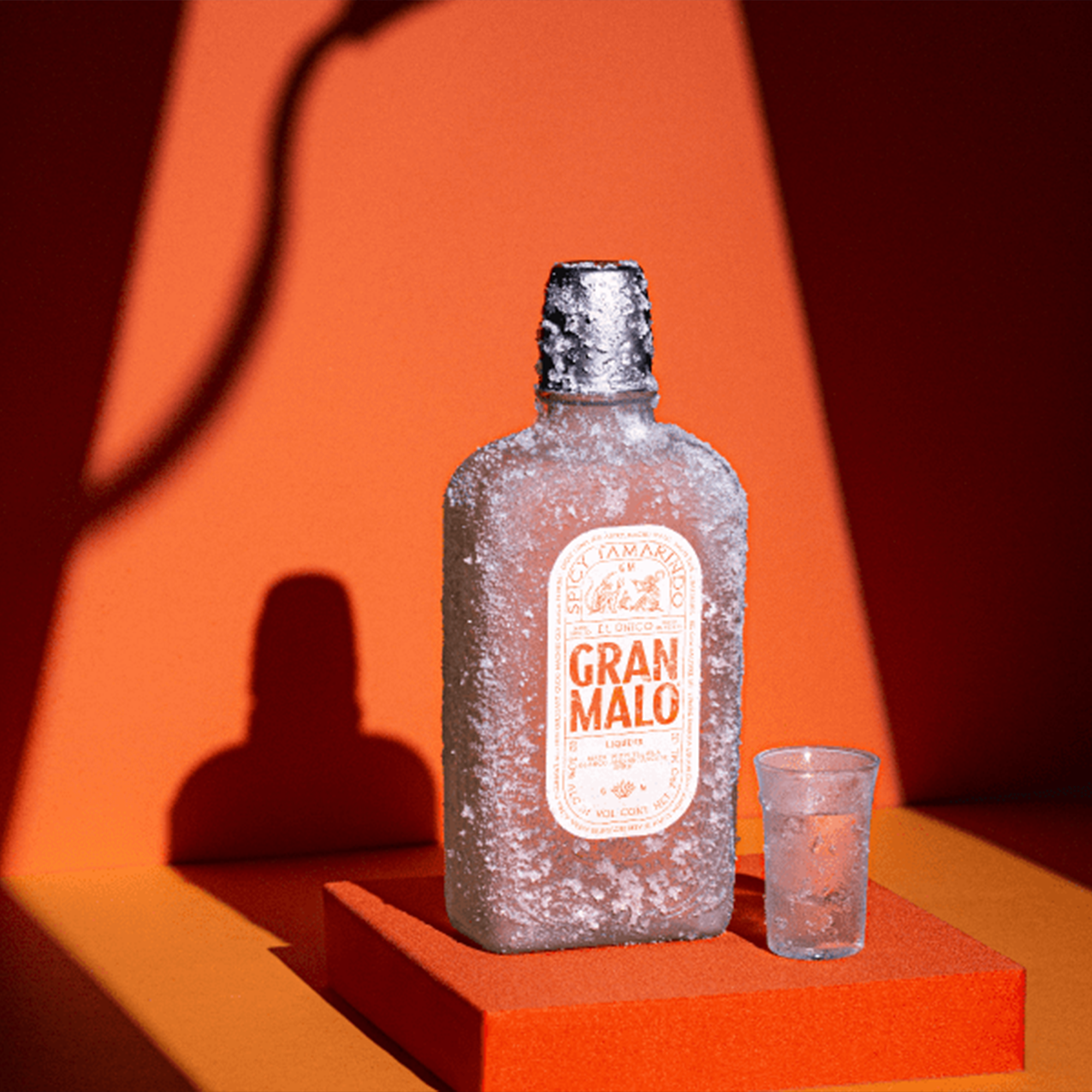 Gran Malo Spicy Tamarindo Tequila Liqueur bottle with shot glass on vibrant orange background.