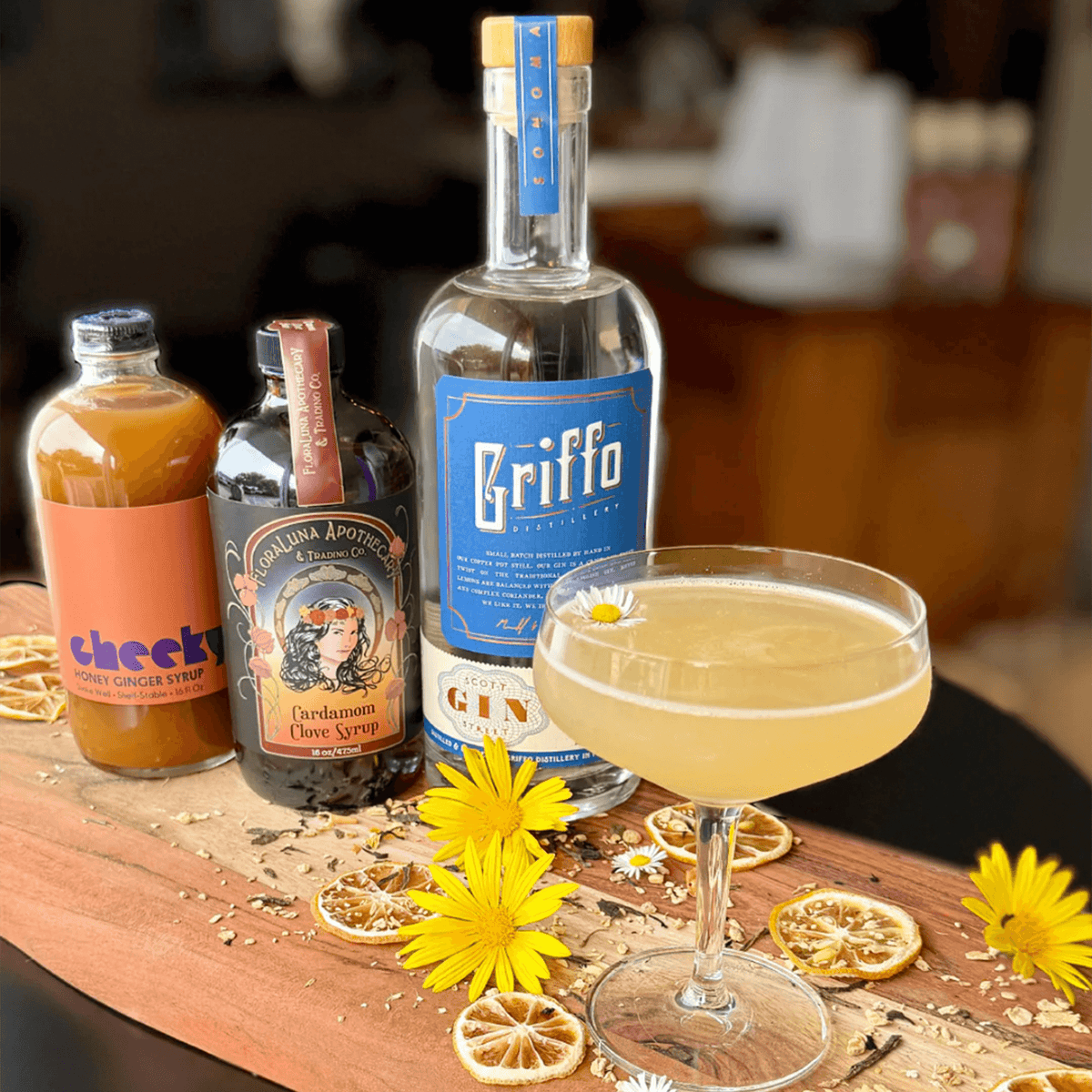 Griffo Scott Street Gin with honey ginger syrup and cardamom clove syrup on a wooden board with garnishes.