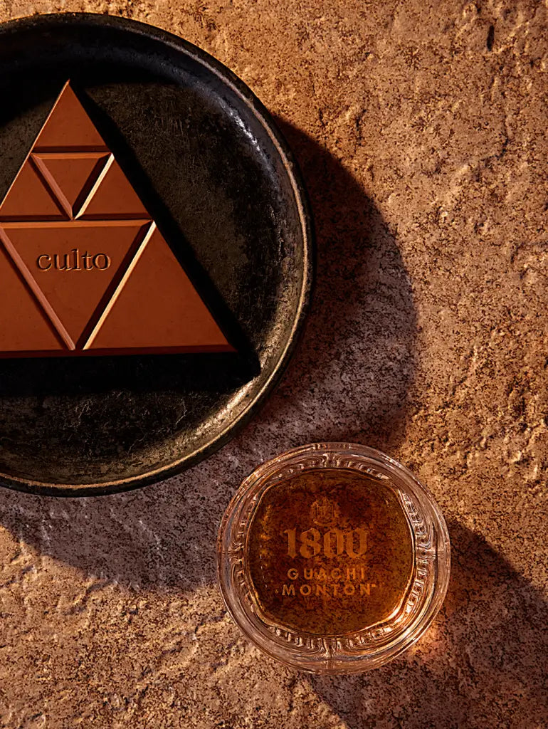 1800 GuachiMonton Añejo Tequila with chocolate pyramid on rustic surface.