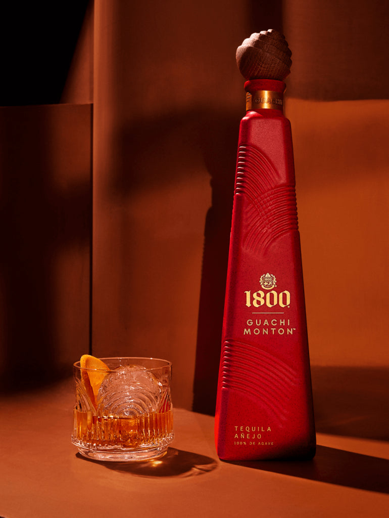 1800 Guachi Monton Añejo Tequila bottle with an elegant glass and orange garnish on a warm backdrop.