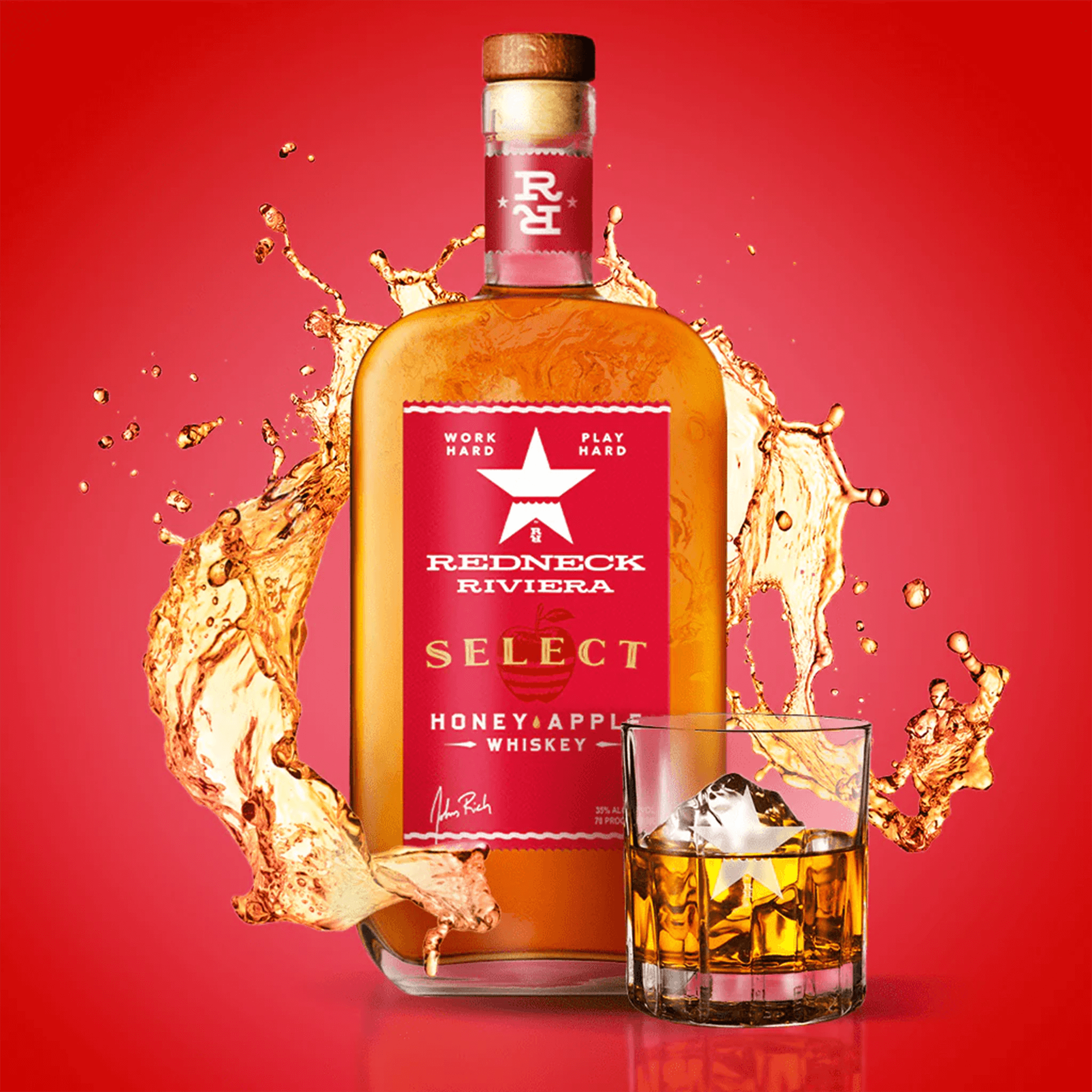 Redneck Riviera Select Honey Apple Whiskey bottle with splash effects and glass on red background.