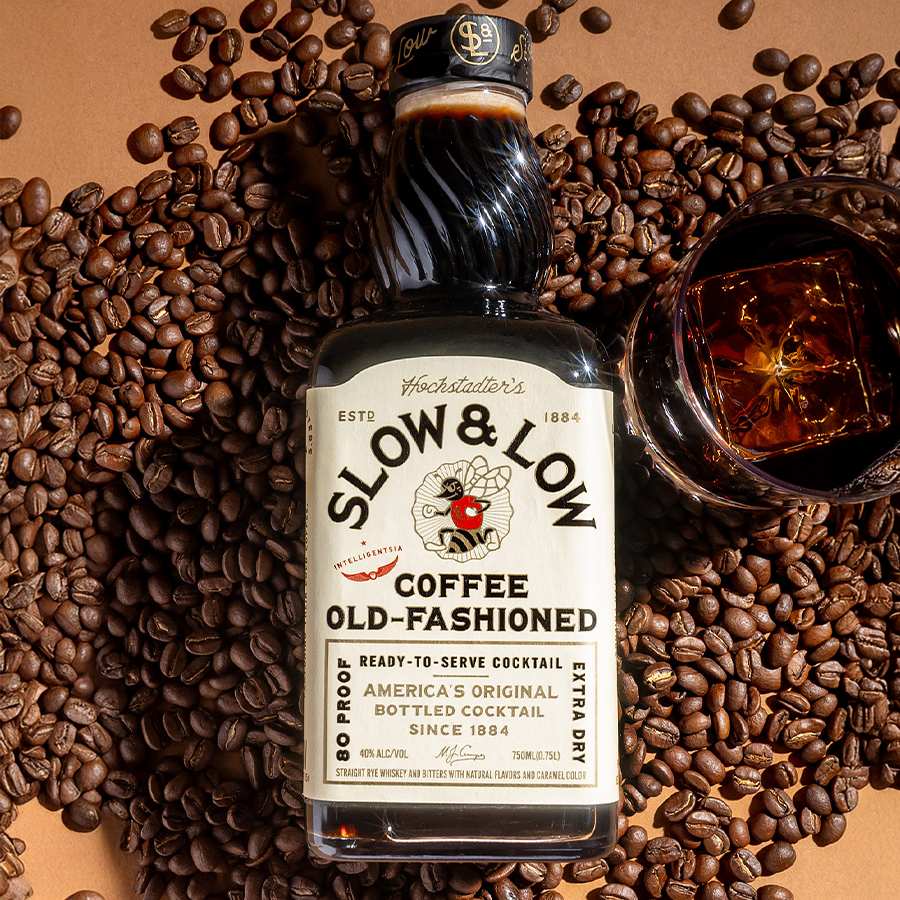 Hochstadter's Slow & Low Coffee Old Fashioned bottle surrounded by coffee beans with a cocktail glass.