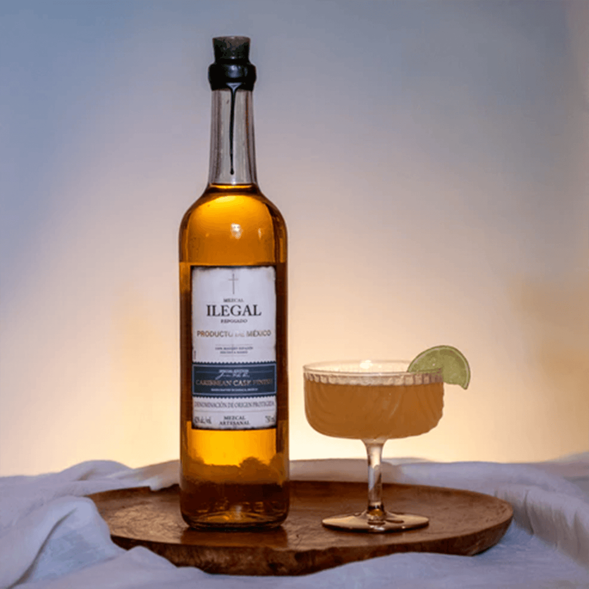 Ilegal Reposado Caribbean Cask Finish Mezcal bottle with cocktail garnished with lime, showcasing the luxurious spirit.