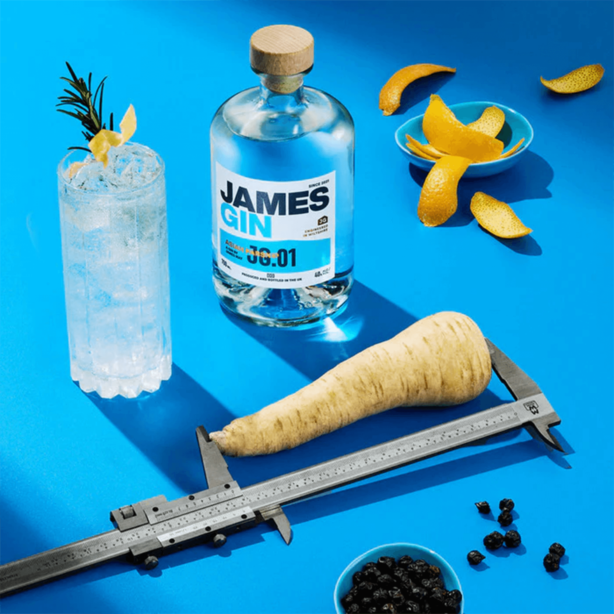 James Gin Asian Parsnip bottle, parsnip, cocktail, and garnishes on a vibrant blue background.