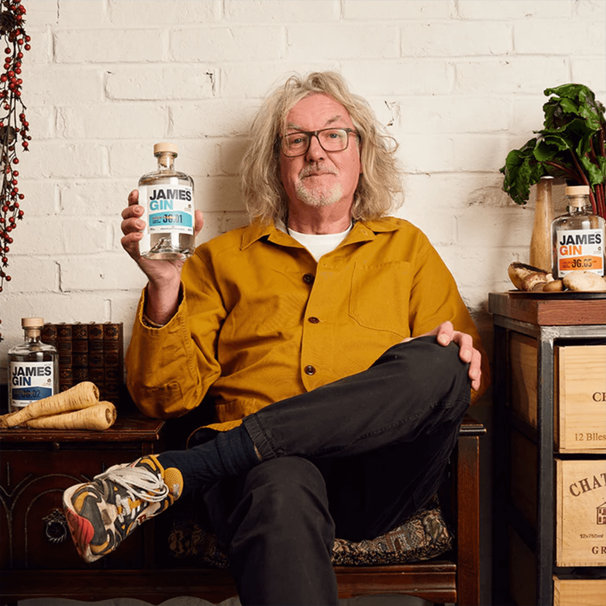 Man holding James Gin Asian Parsnip bottle, seated in a cozy setting with parsnips and vintage decor.