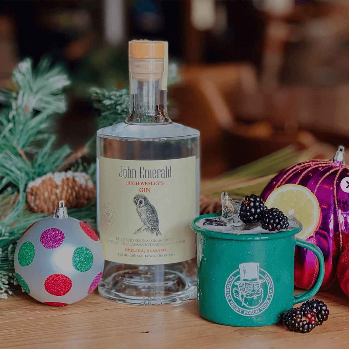 Bottle of John Emerald Hugh Wesley's Gin with festive decor and a cocktail garnished with blackberries.