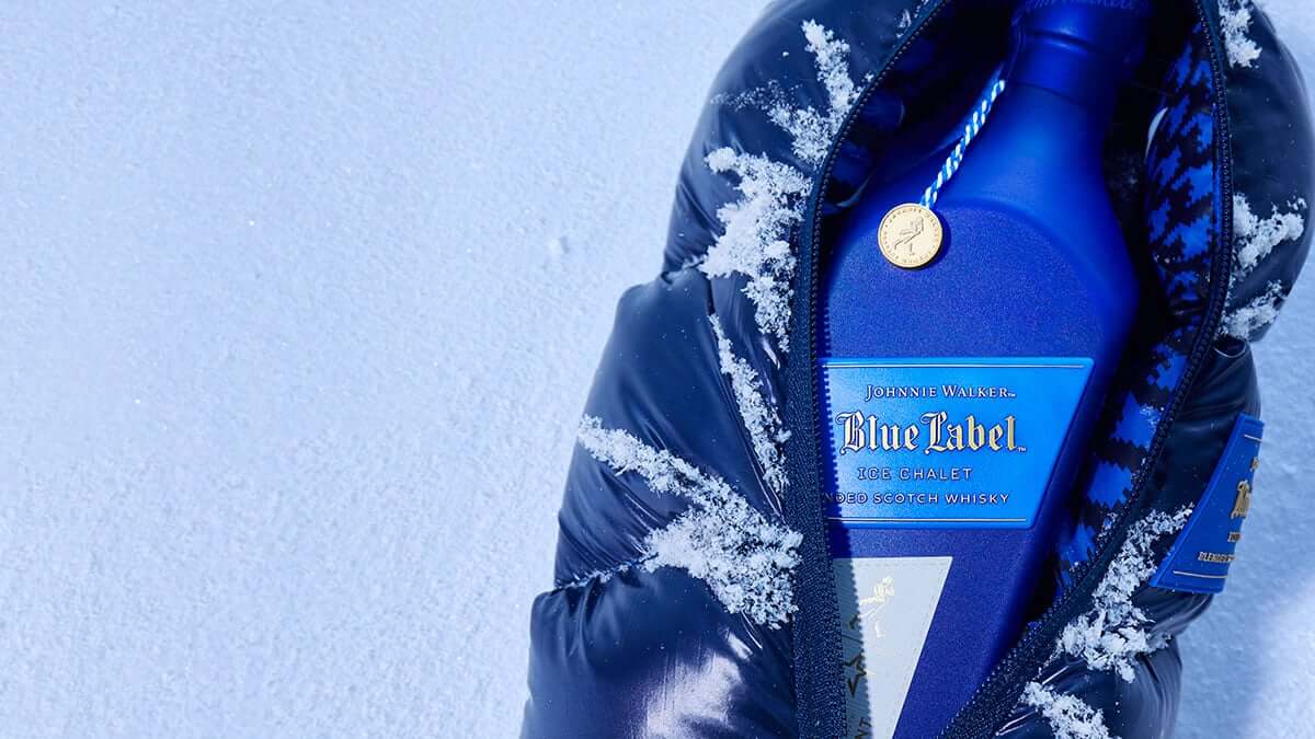 Johnnie Walker Blue Label Ice Chalet whisky in a stylish padded jacket on snowy background, highlighting luxury and winter vibes.
