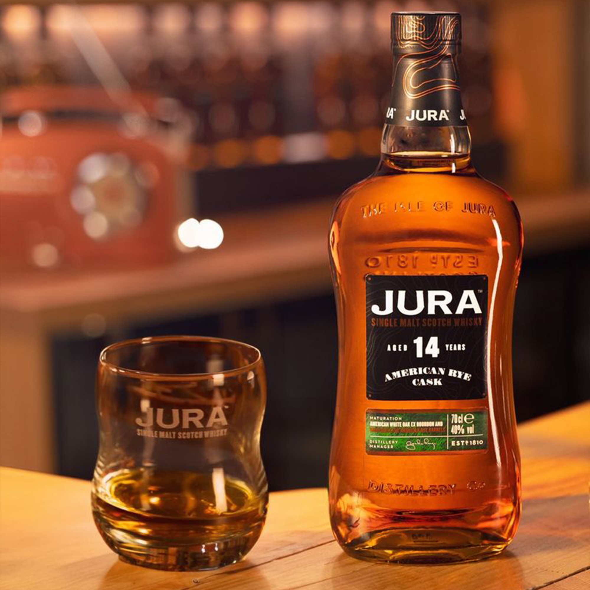 Jura 14 Year American Rye Cask whiskey bottle and glass on a wooden bar, highlighting rich flavors.