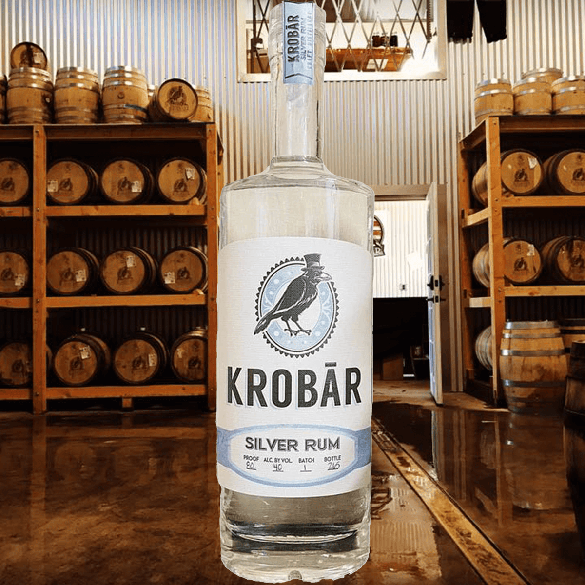 Krobar Silver Rum bottle on display in a distillery with oak barrels in the background, showcasing premium craftsmanship.