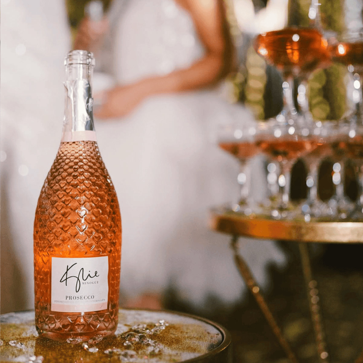 Kylie Minogue Prosecco Rosé bottle with sparkling glasses in a festive setting, showcasing vibrant pink color and elegance.
