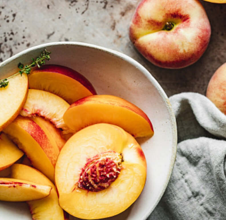 Fresh, sliced peaches in a bowl, showcasing vibrant colors and juicy textures perfect for Bird Dog Peach Whiskey.