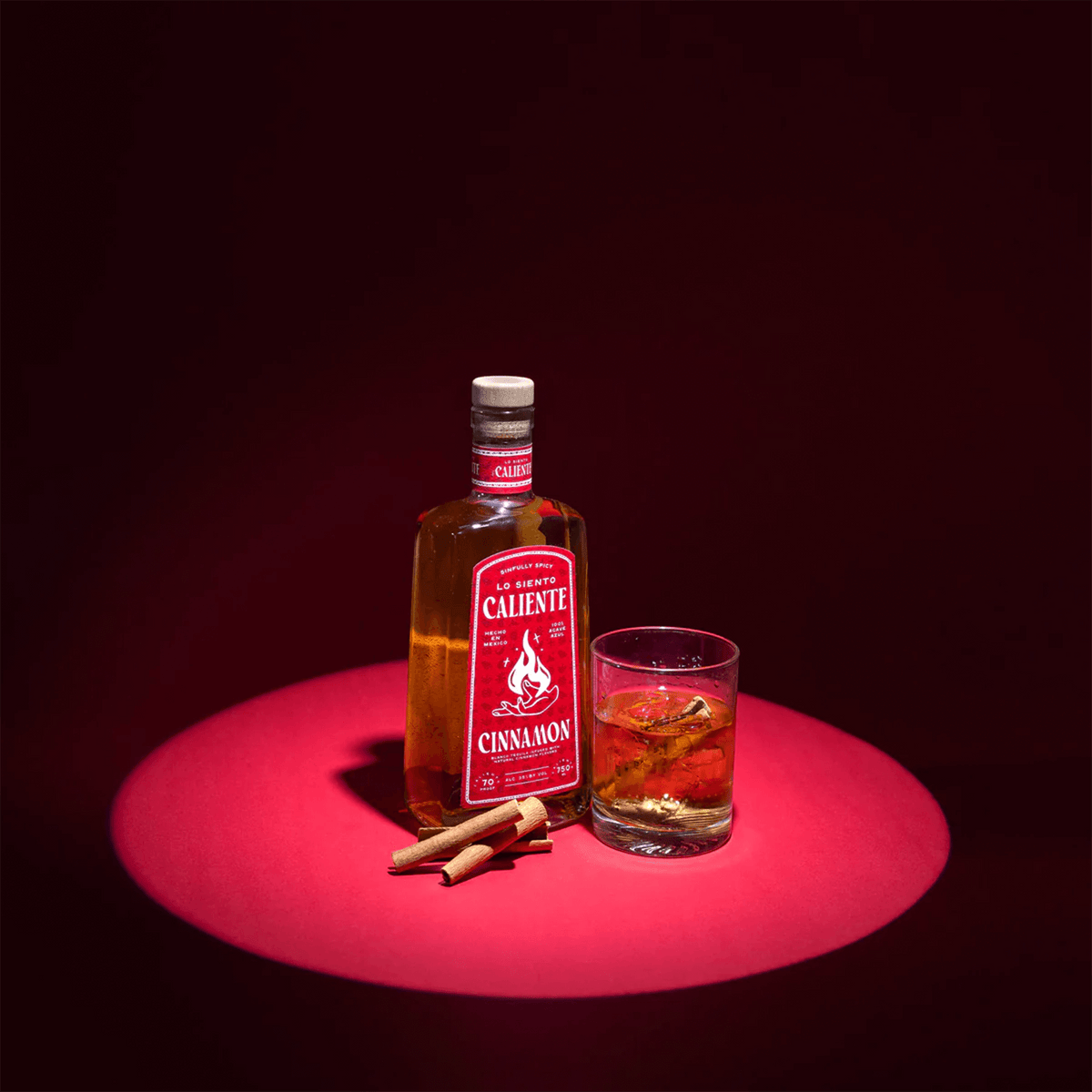 Lo Siento Caliente Cinnamon Tequila bottle with a glass and cinnamon sticks on a vibrant background.