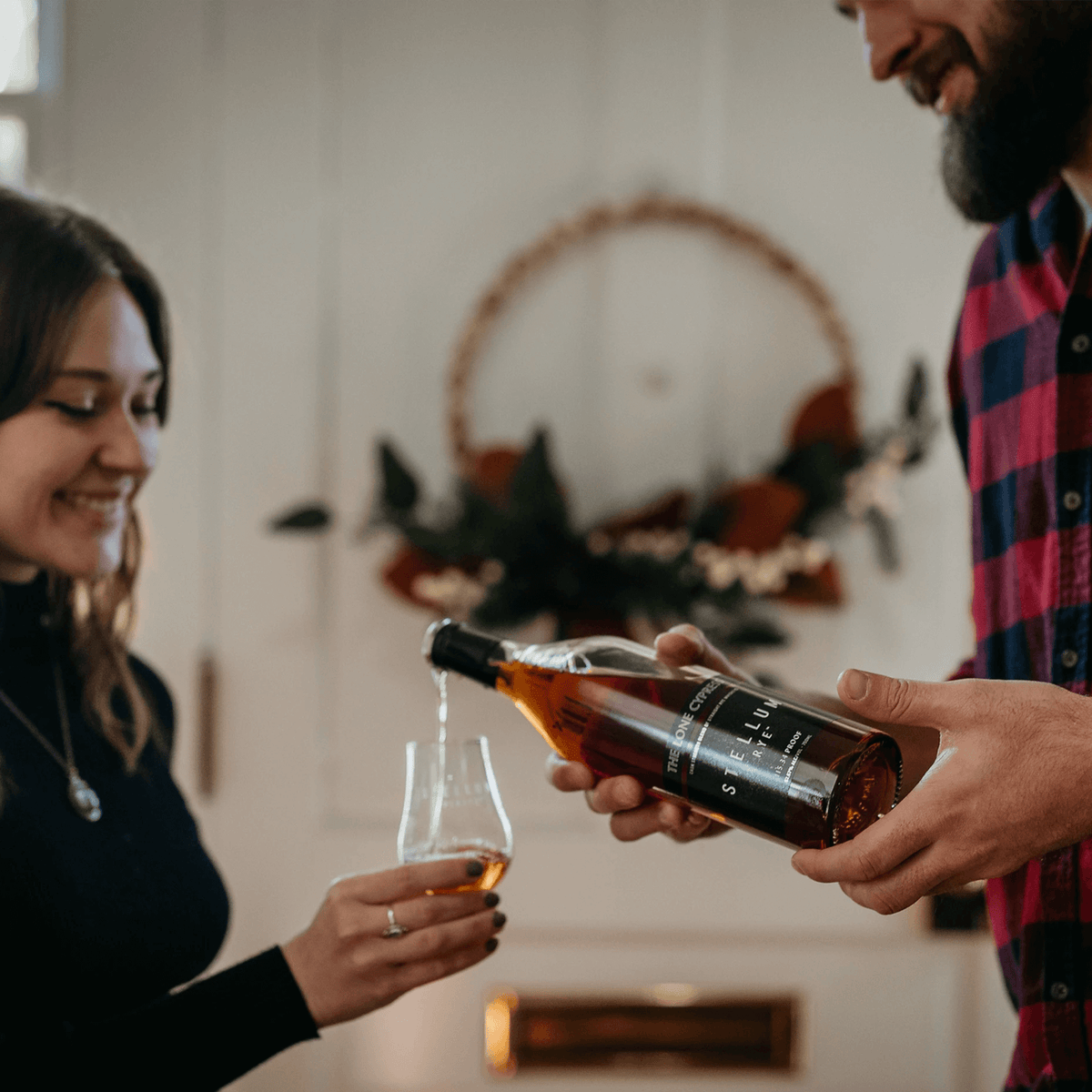 Couple enjoying Stellum Fibonacci Blend #1 cask strength rye whiskey in a cozy setting.