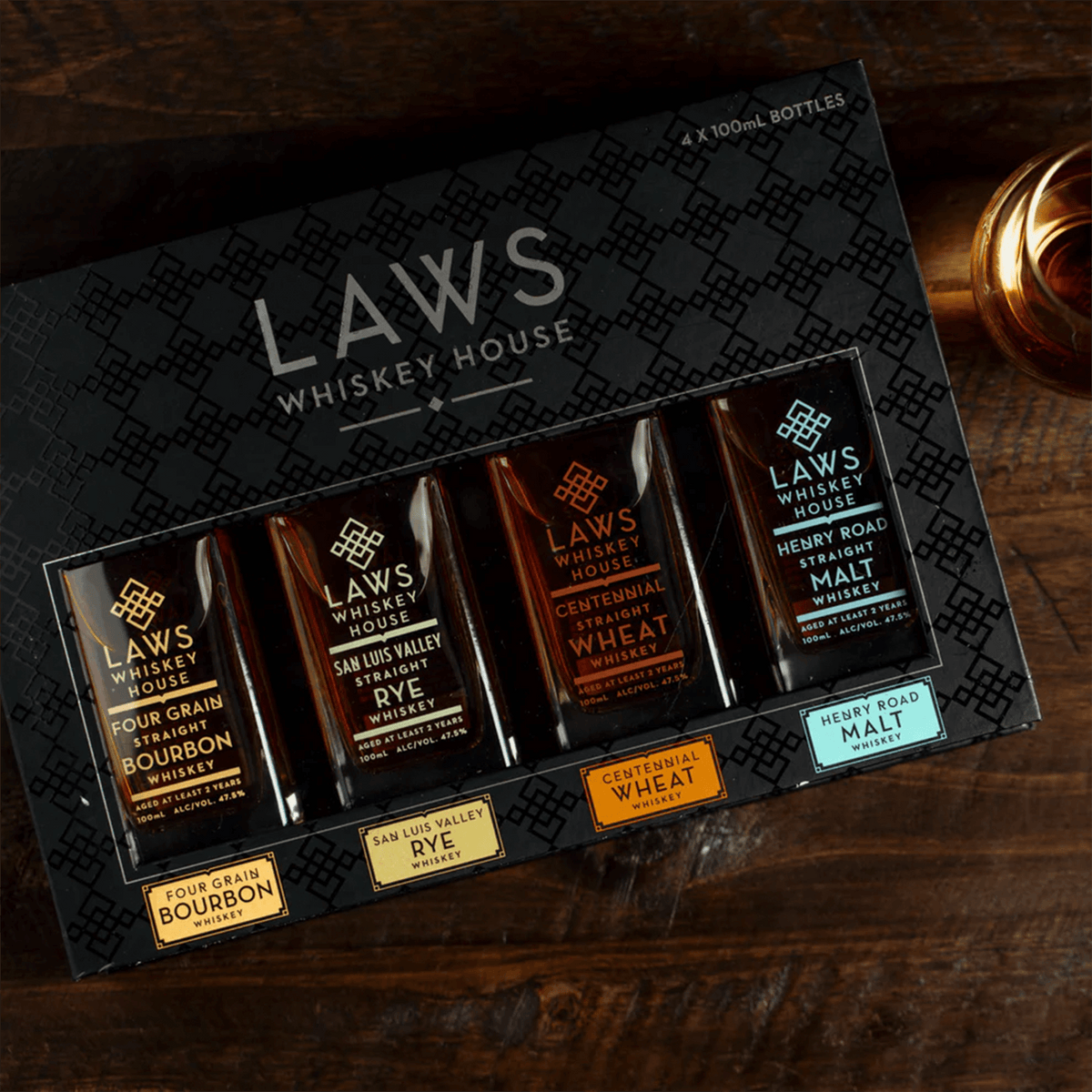 Laws Whiskey House four-pack gift set with 100ml bottles of bourbon, rye, wheat, and malt whiskeys on a wooden table.