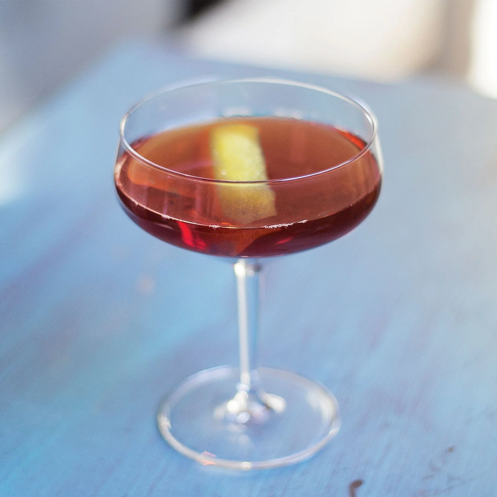 Stylish cocktail in a coupe glass with a lemon twist on a light blue table.