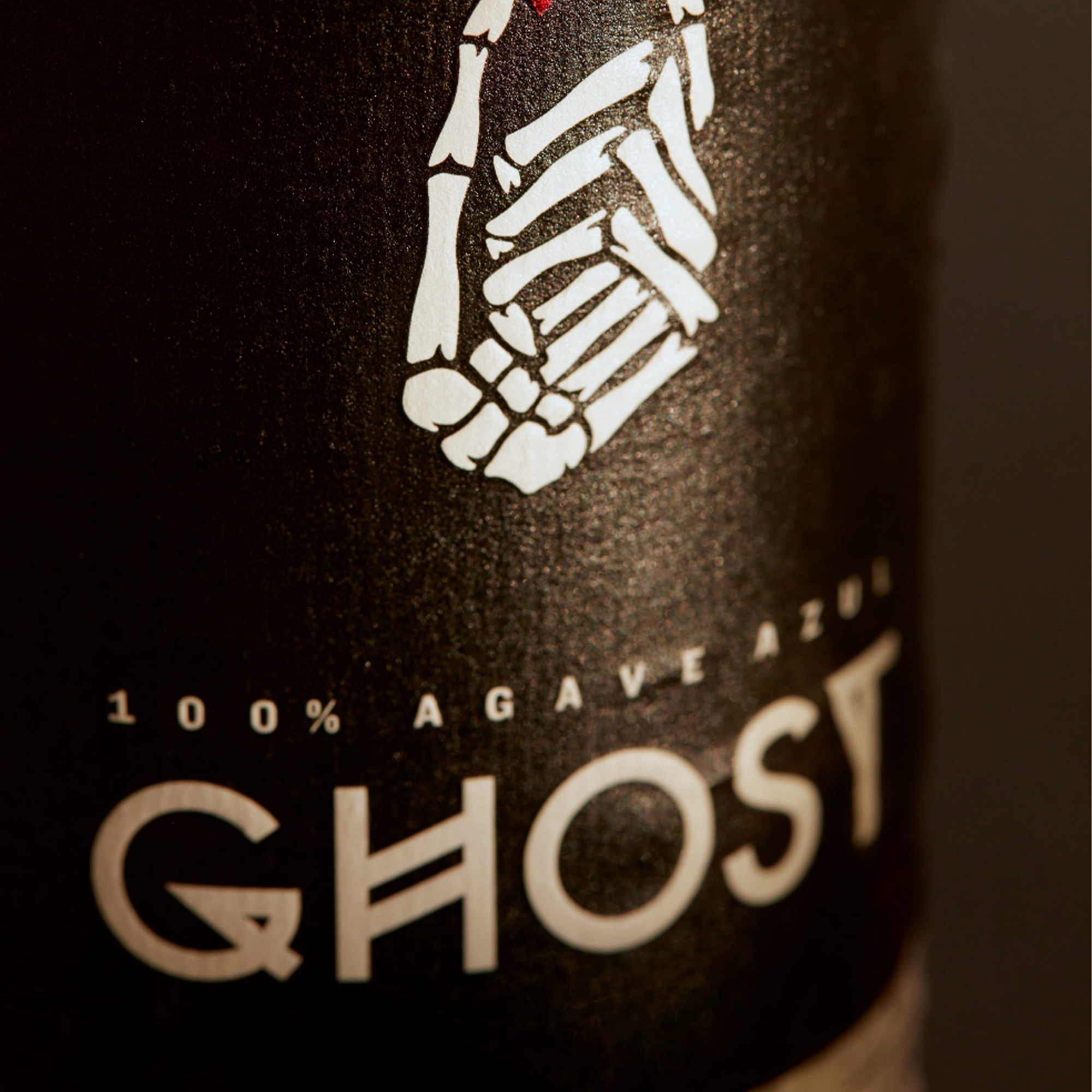 Close-up of Ghost Spicy Reposado Tequila label featuring skeleton hand and '100% Agave Azul' text.