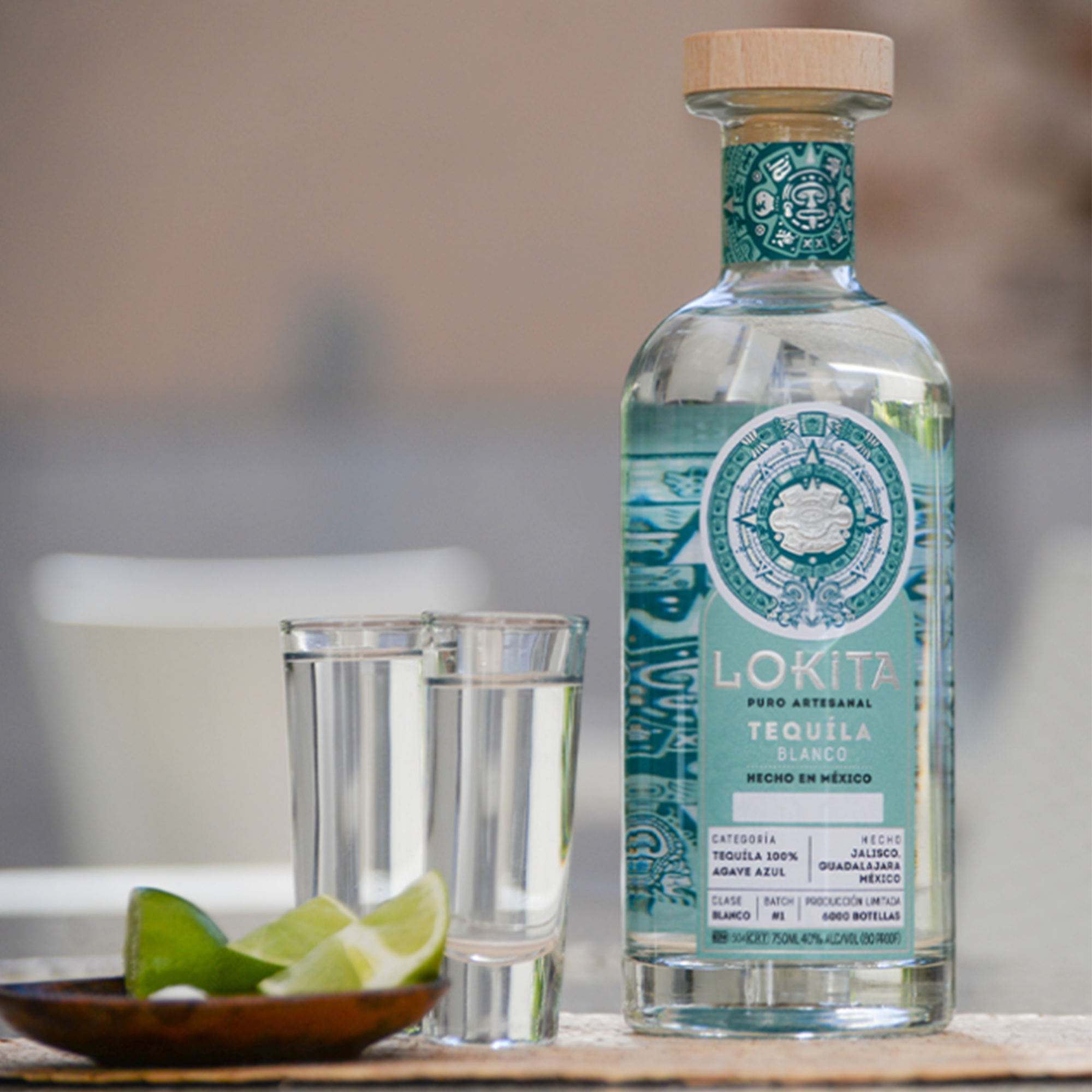 Lokita Blanco Tequila bottle with shot glasses and lime on a table, showcasing premium 100% agave craftsmanship.