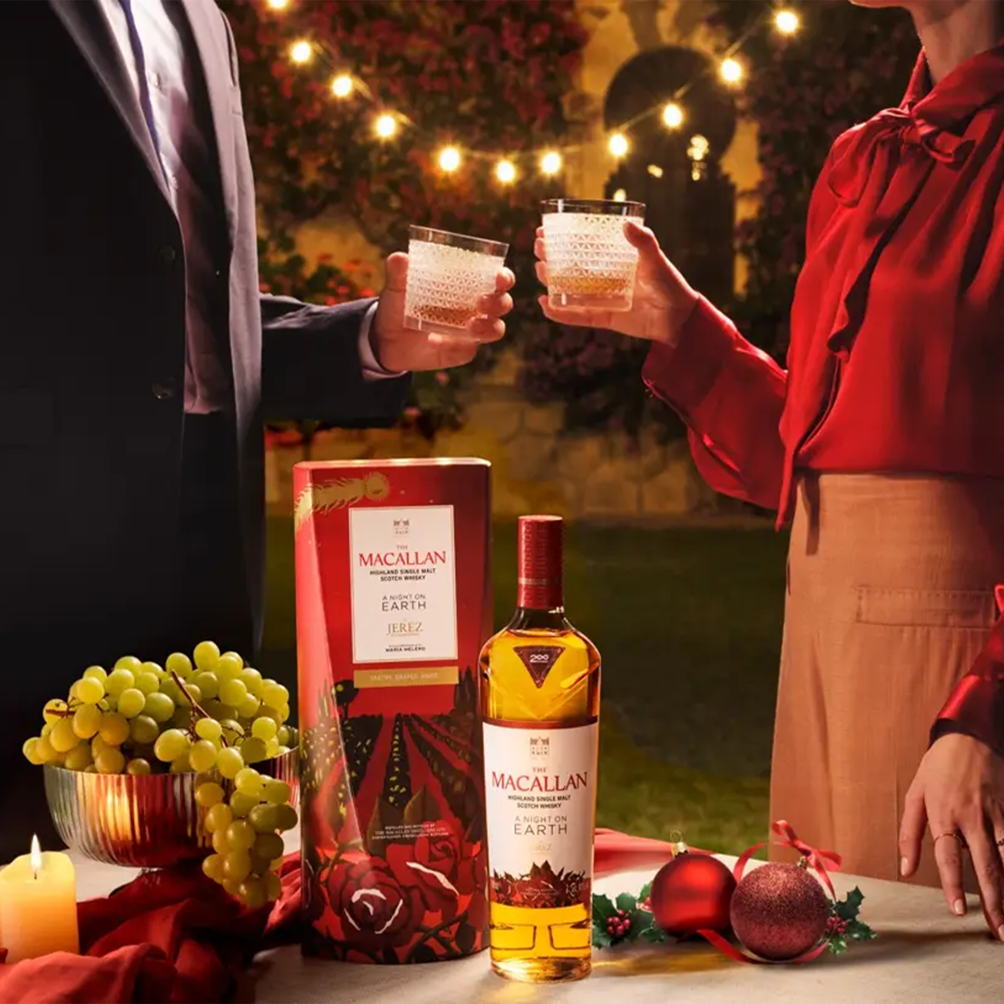 Couple toasting with Macallan A Night On Earth Jerez De La Frontera Scotch in festive setting with grapes and holiday decor.