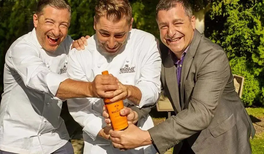 Three chefs joyfully celebrating with a bottle of Macallan Edition No. 2 in a sunny outdoor setting.