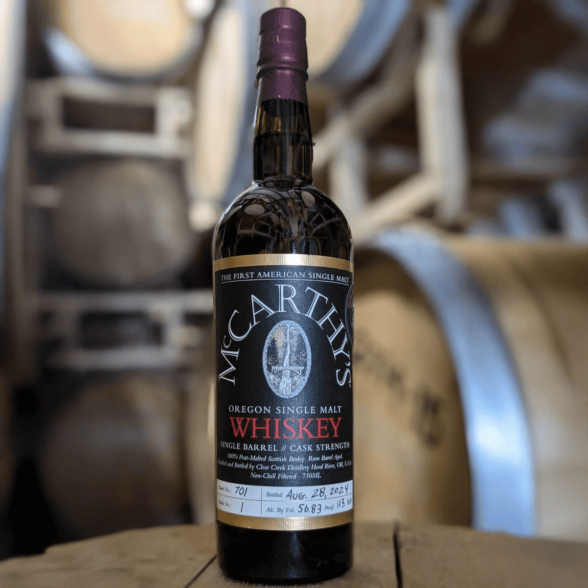 McCarthy's Single Barrel Cask Strength 6 Year Single Malt Whiskey bottle in distillery with barrels in background.
