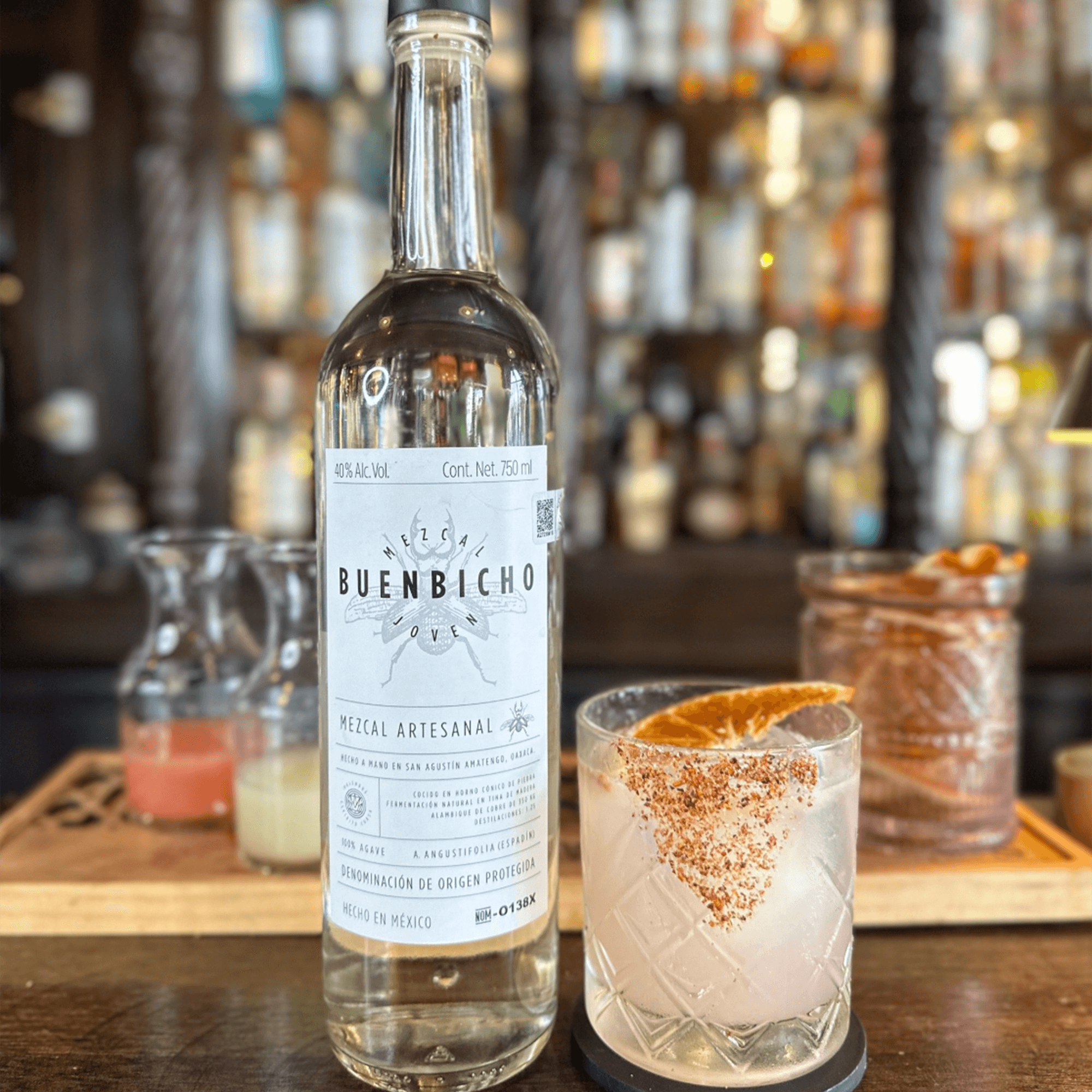 Bottle of Buen Bicho Mezcal Artesanal with a cocktail glass, showcasing sustainable Mexican craftsmanship.