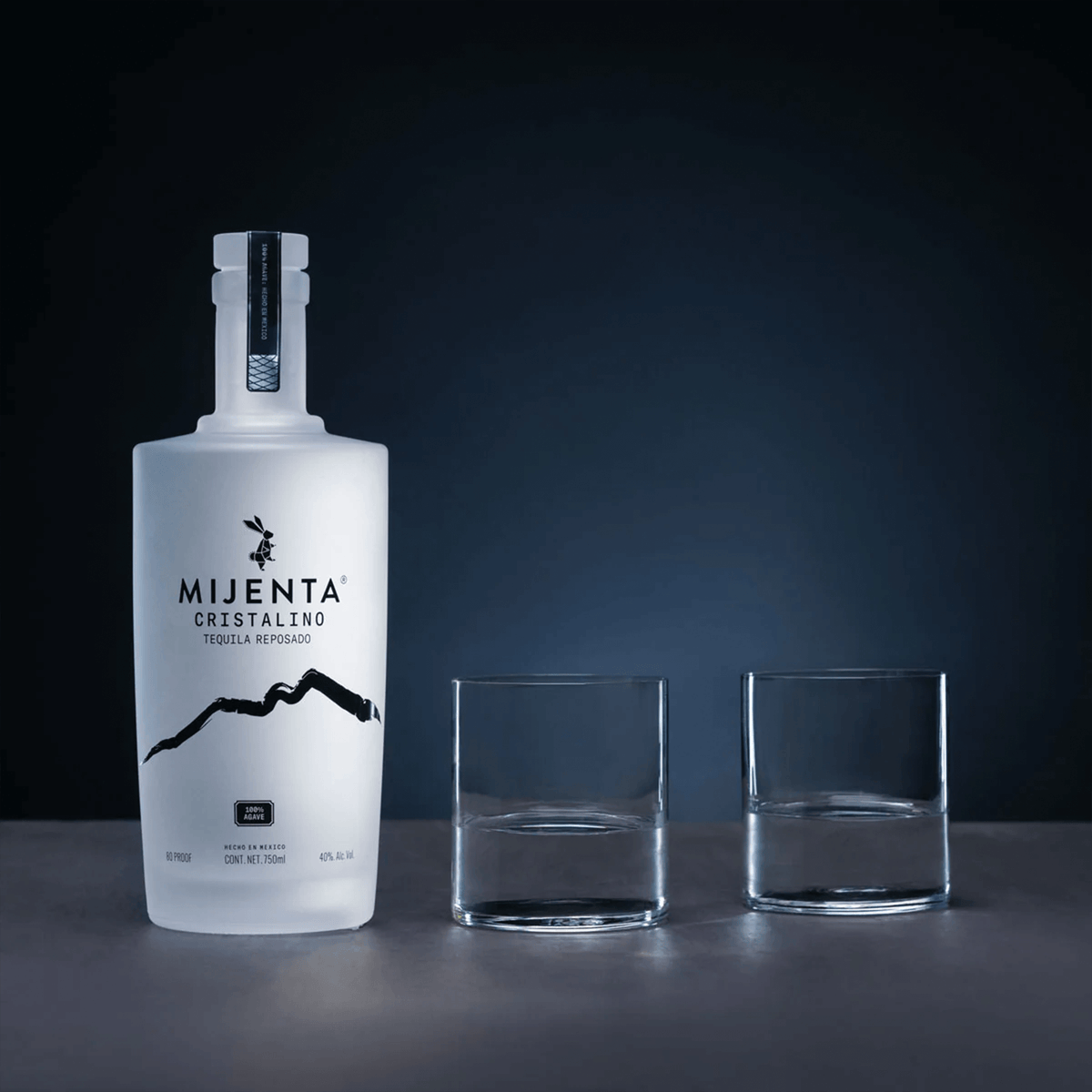 Mijenta Cristalino Tequila bottle with two glasses on a dark background, showcasing its unique design and elegance.