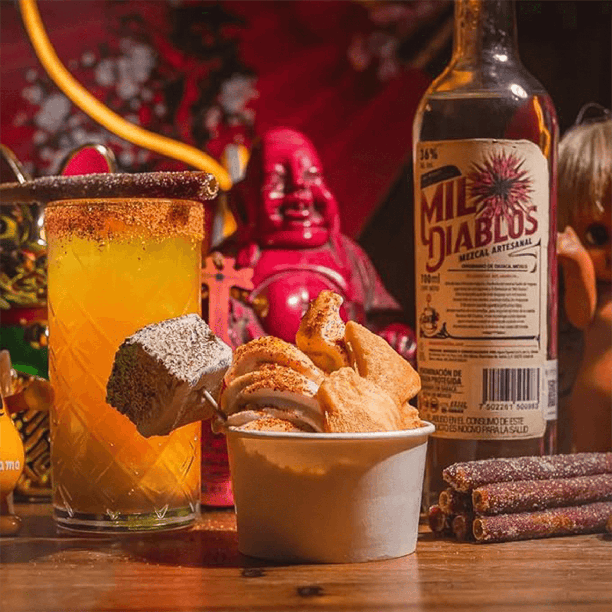 Mil Diablos Mezcal bottle with cocktail and snacks in vibrant, festive setting.