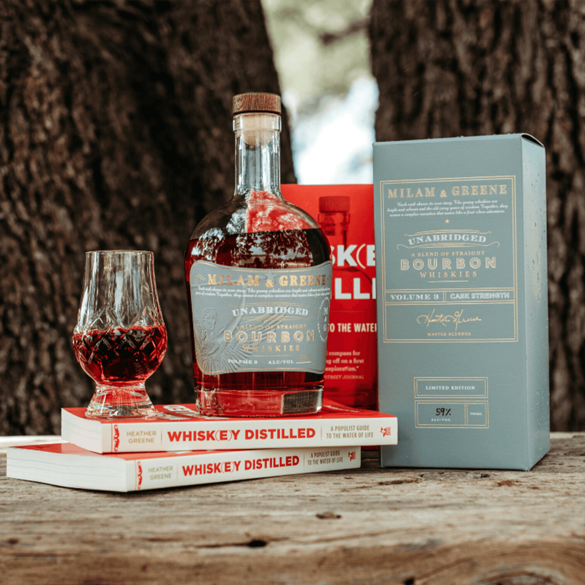 Milam & Greene Unabridged Volume 3 Straight Bourbon Whiskey with glass and books on a wooden table.