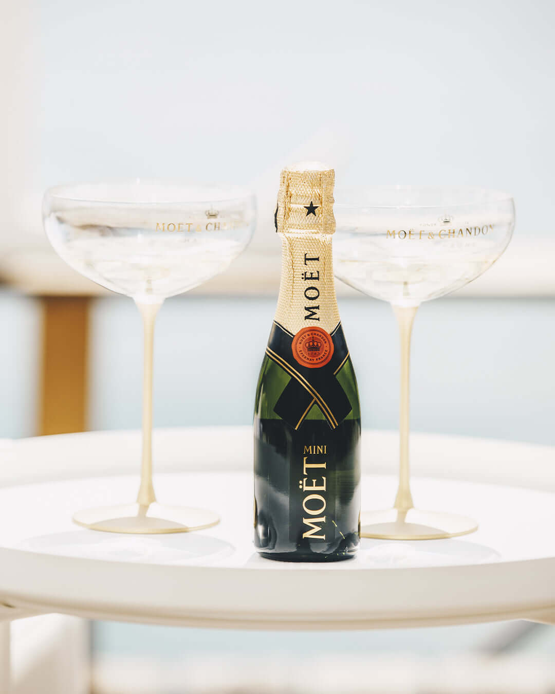 Mini Moët & Chandon Brut Impérial bottle with elegant champagne glasses on a table.