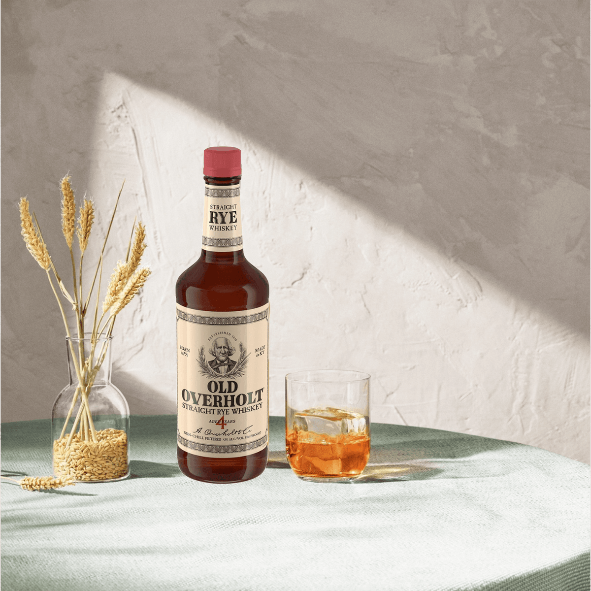 Old Overholt 4 Year Straight Rye whiskey bottle with a glass and wheat in a serene setting, showcasing robust flavor and spices.
