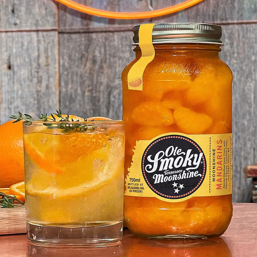 Jar of Ole Smoky Mandarins Moonshine with a refreshing drink and citrus garnishes.