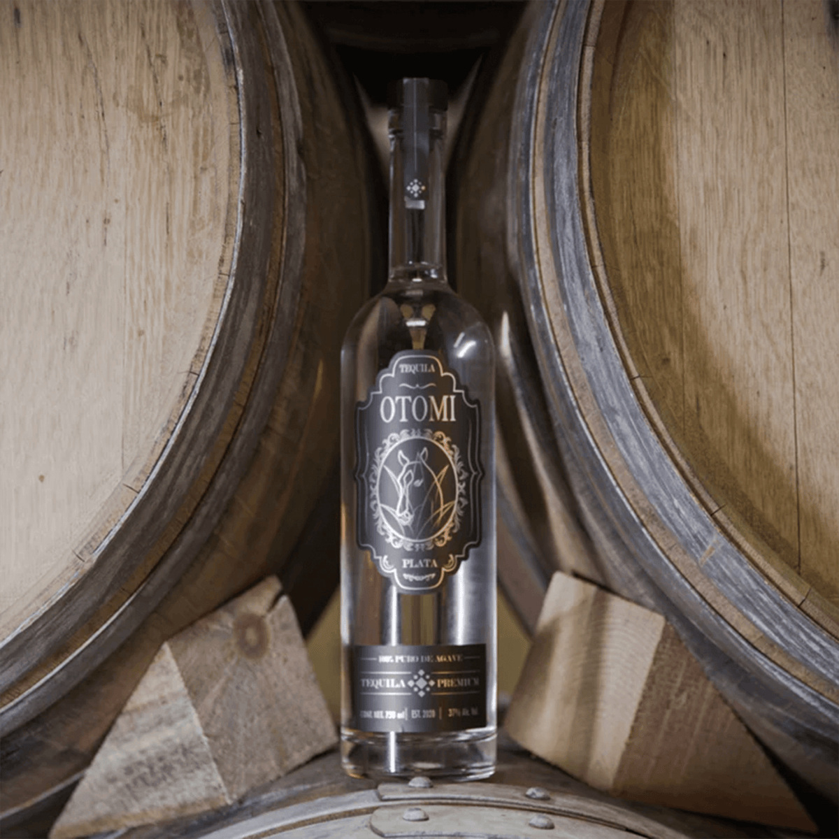 Otomi Silver Tequila bottle showcased between wooden barrels, highlighting its craftsmanship and heritage.