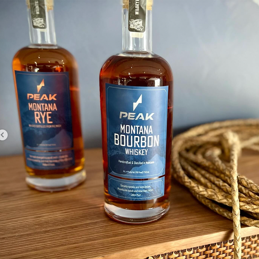 Two bottles of Peak Montana Rye and Peak Montana Bourbon Whiskey displayed together on a wooden table.