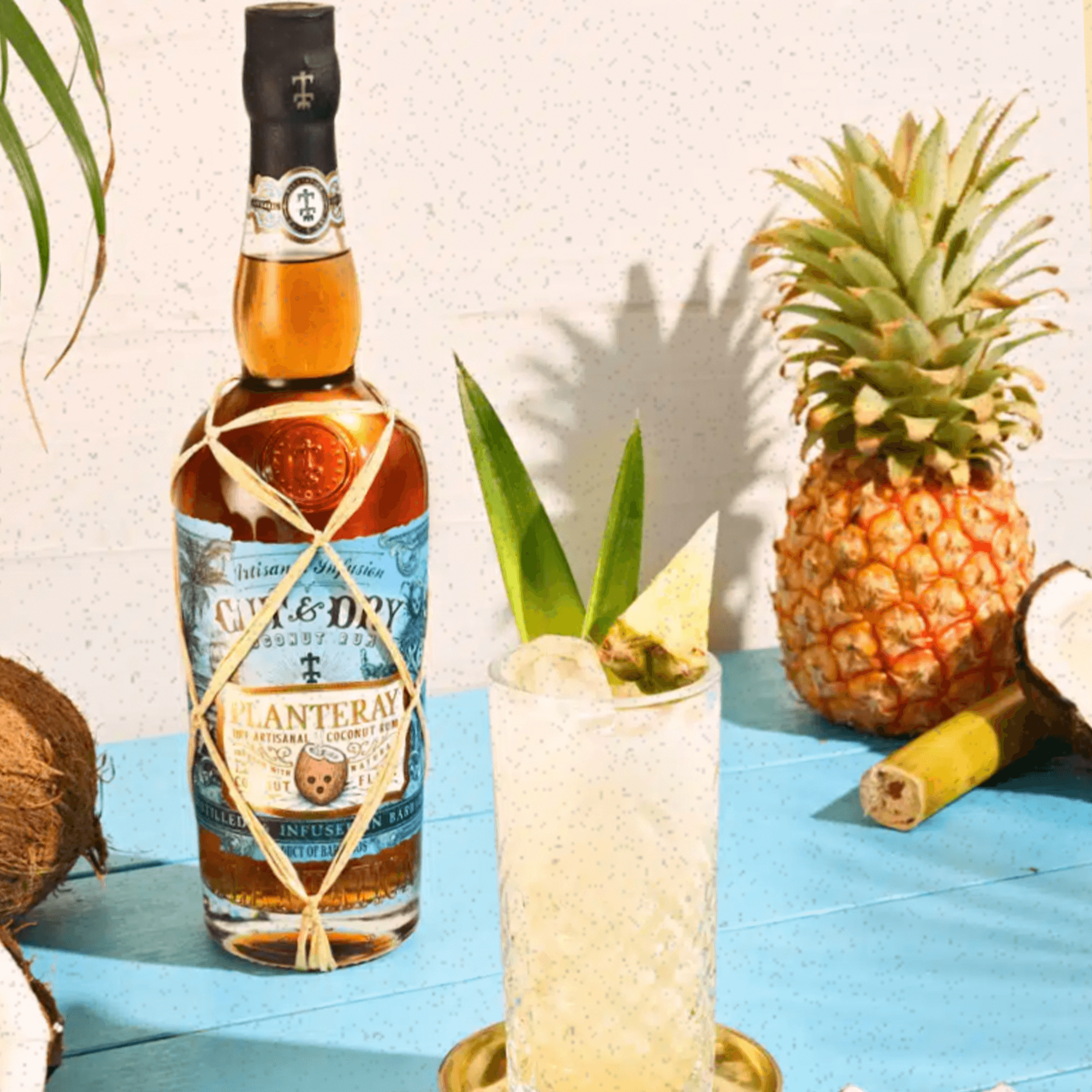 Planteray Cut & Dry Coconut Rum bottle with cocktail and tropical fruits on a vibrant blue table.