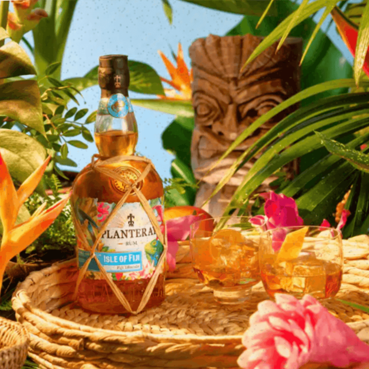 Planteray Double Barrel Isle of Fiji Rum bottle surrounded by tropical flowers and tiki statue, showcasing Fijian beauty.
