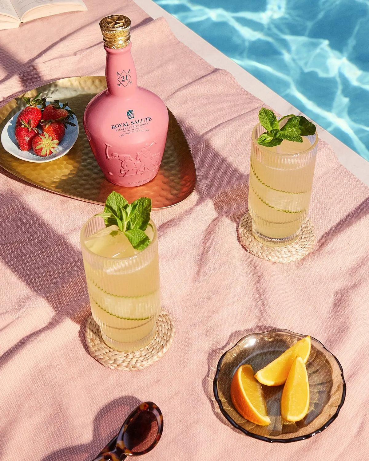 Royal Salute The Miami Polo Edition bottle with cocktails, mint, and fruits on a sunlit beach setting.