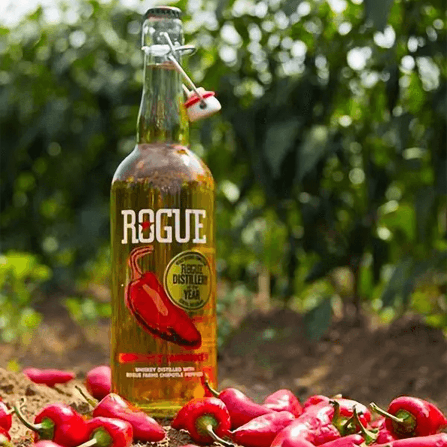 Rogue Chipotle Flavored Whiskey bottle with jalapeños in a lush farm setting.