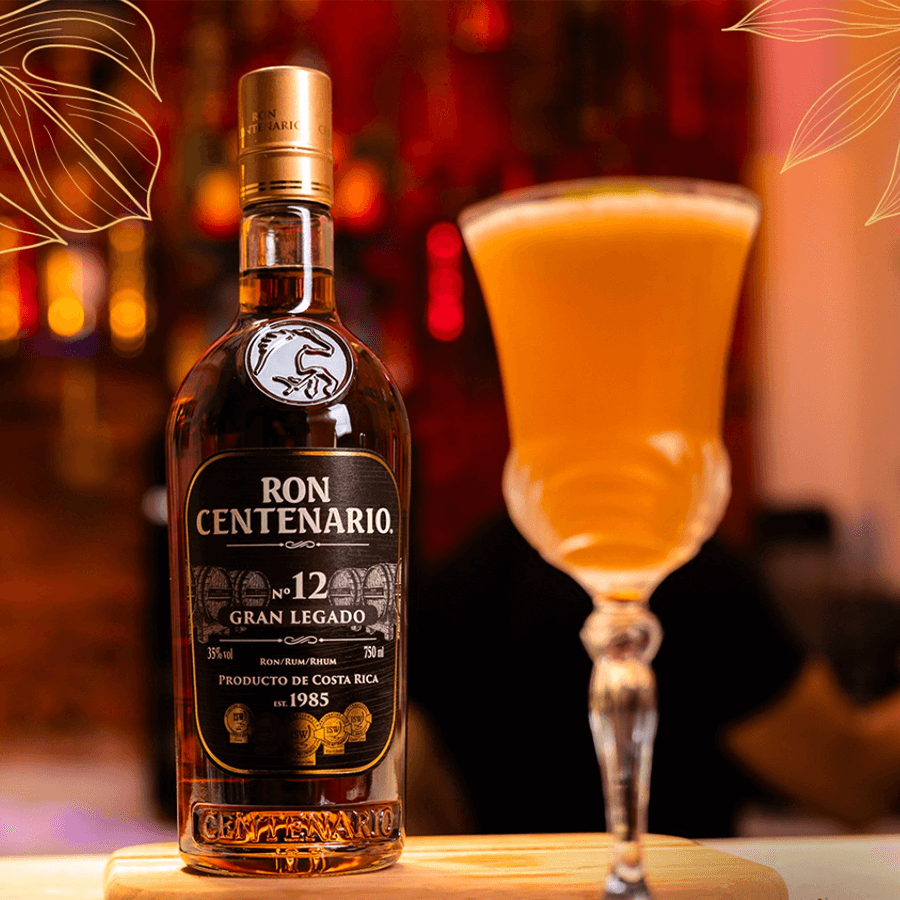Bottle of Ron Centenario 12 Year Gran Legado Rum alongside a tall cocktail glass filled with a golden drink.