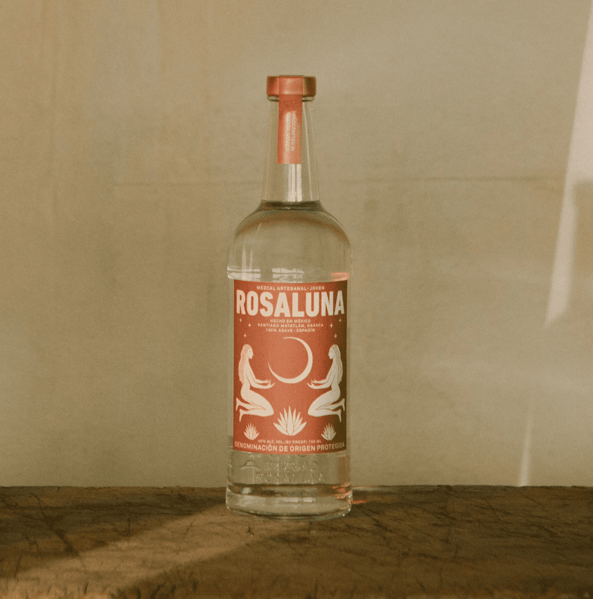 Rosaluna Joven Artesanal Mezcal bottle showcasing vibrant design and smooth textures on rustic wood surface.