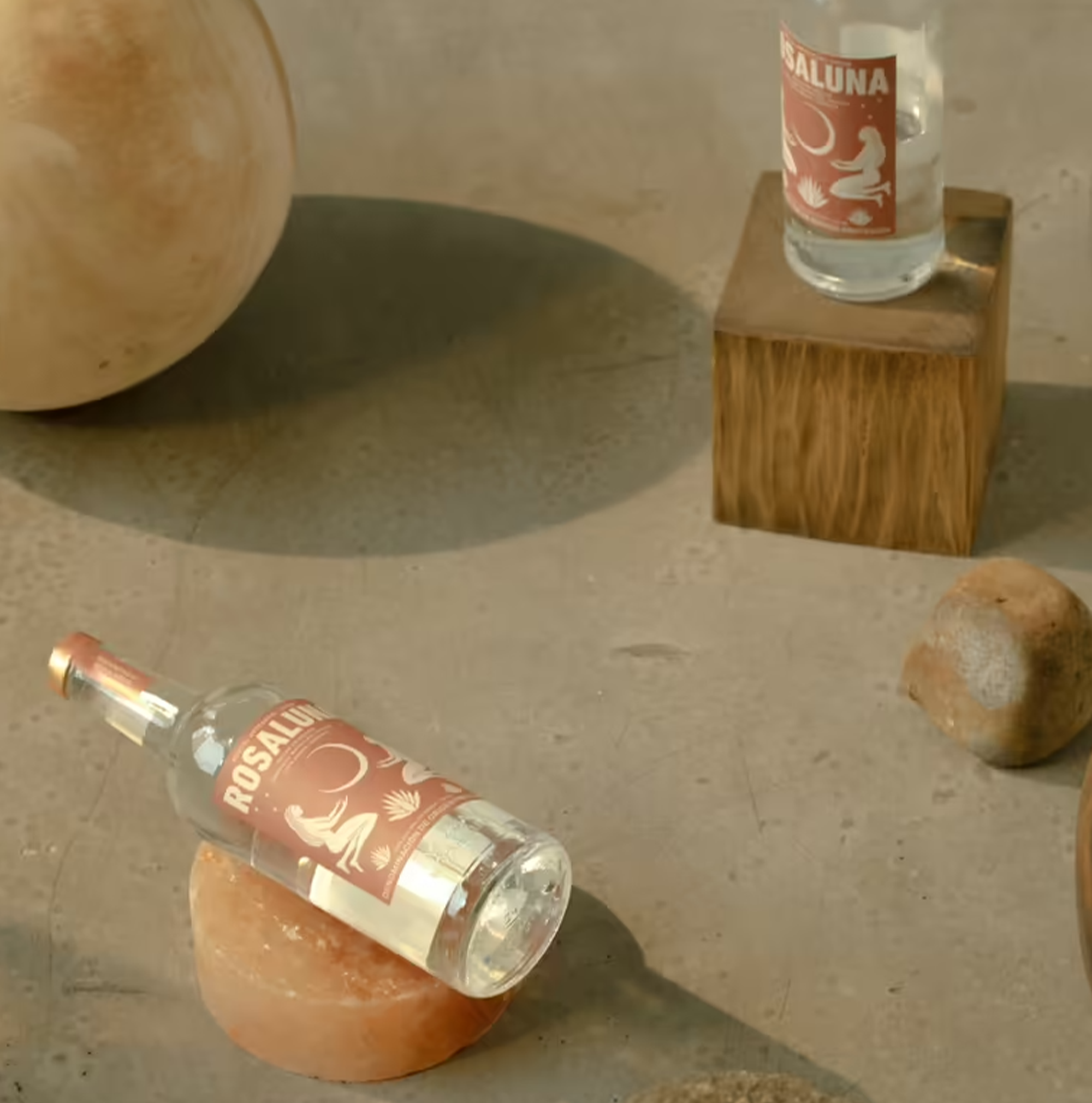 Rosaluna Joven Artesanal Mezcal bottle on display with natural stones, showcasing its vibrant packaging and artisanal quality.