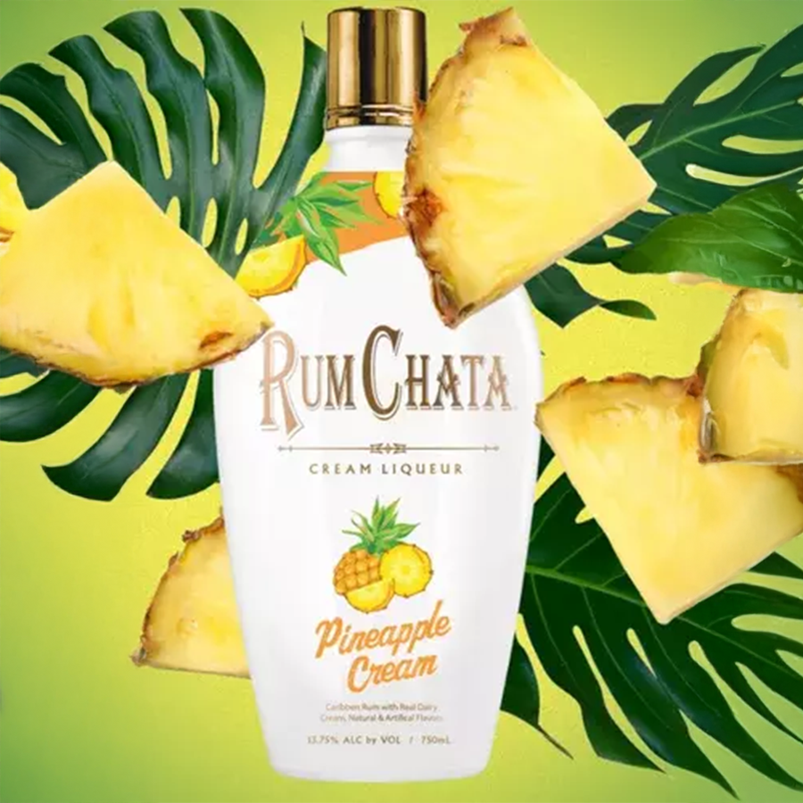 RumChata Pineapple bottle surrounded by pineapple slices and tropical leaves on a vibrant background.