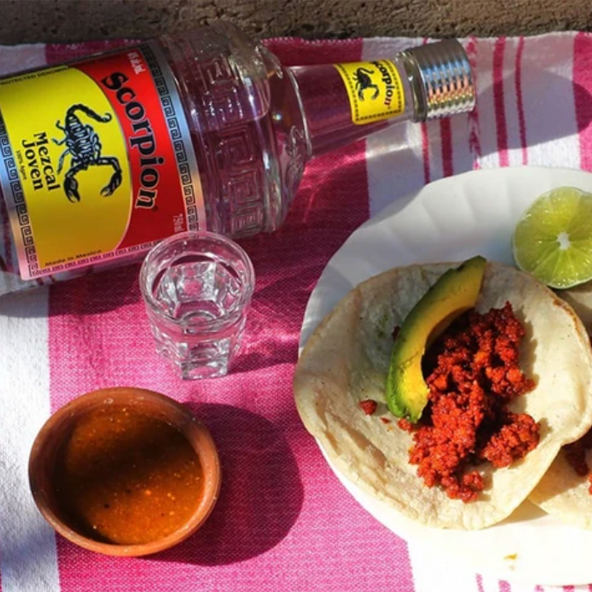 Scorpion Mezcal bottle beside tacos and shot glass on a vibrant tablecloth, showcasing a delicious pairing.